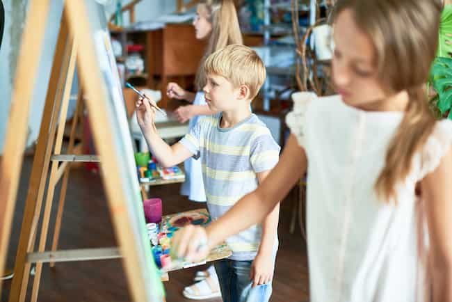 Вид сбоку на группу детей, рисующих на мольбертах во время художественной студии класса, достаточно сосредоточиться на маленьком мальчике.